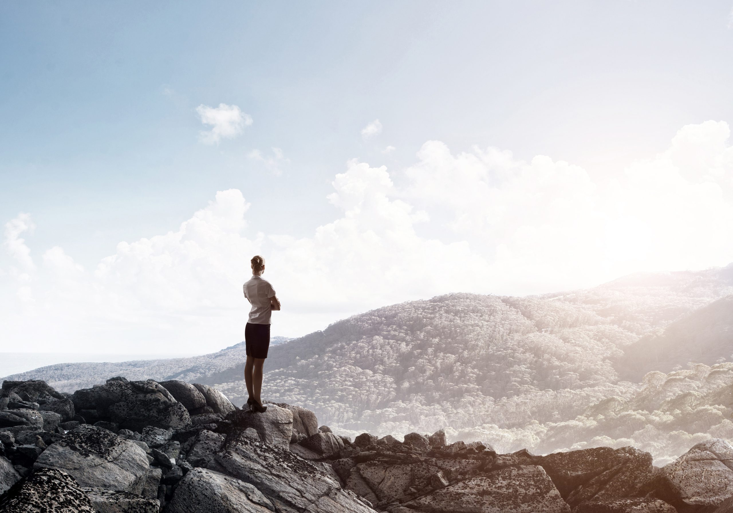 A woman standing on a mountain peak, gazing at the vast valley below.